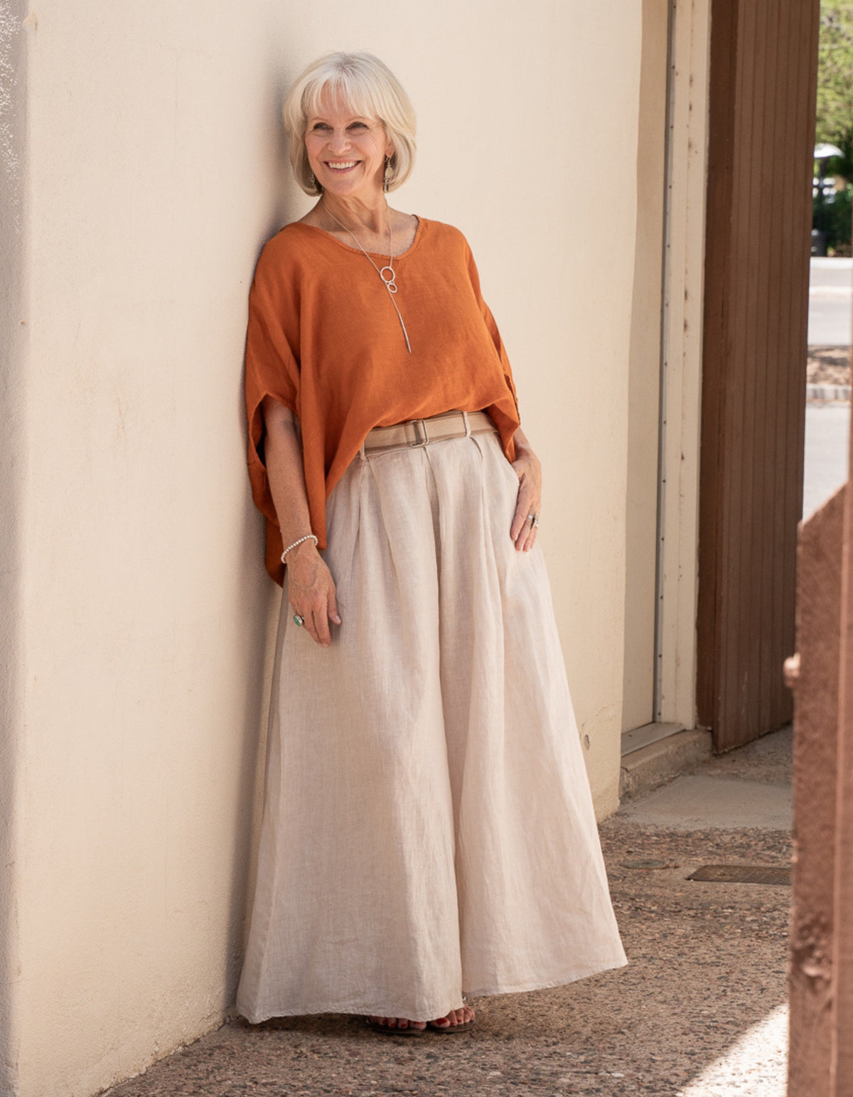Conscious Coterie woman wearing an orange top and beige skirt standing against a wall.