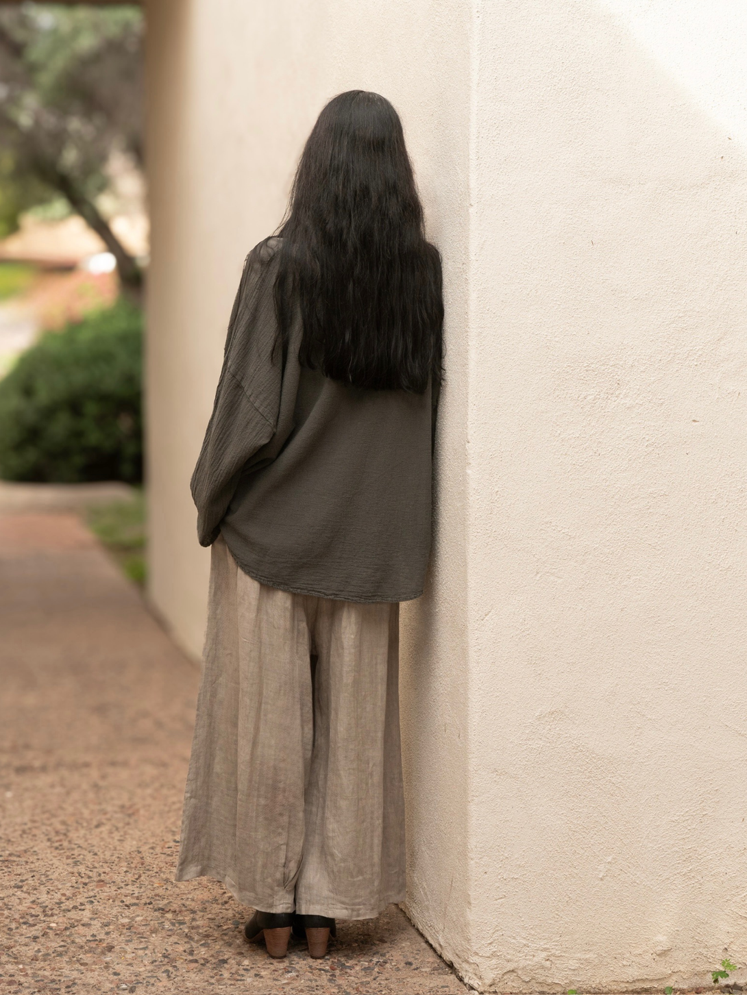 Conscious Coterie Alyssa top in charcoal grey woman facing away showing the back view of the top while leaning against the wall