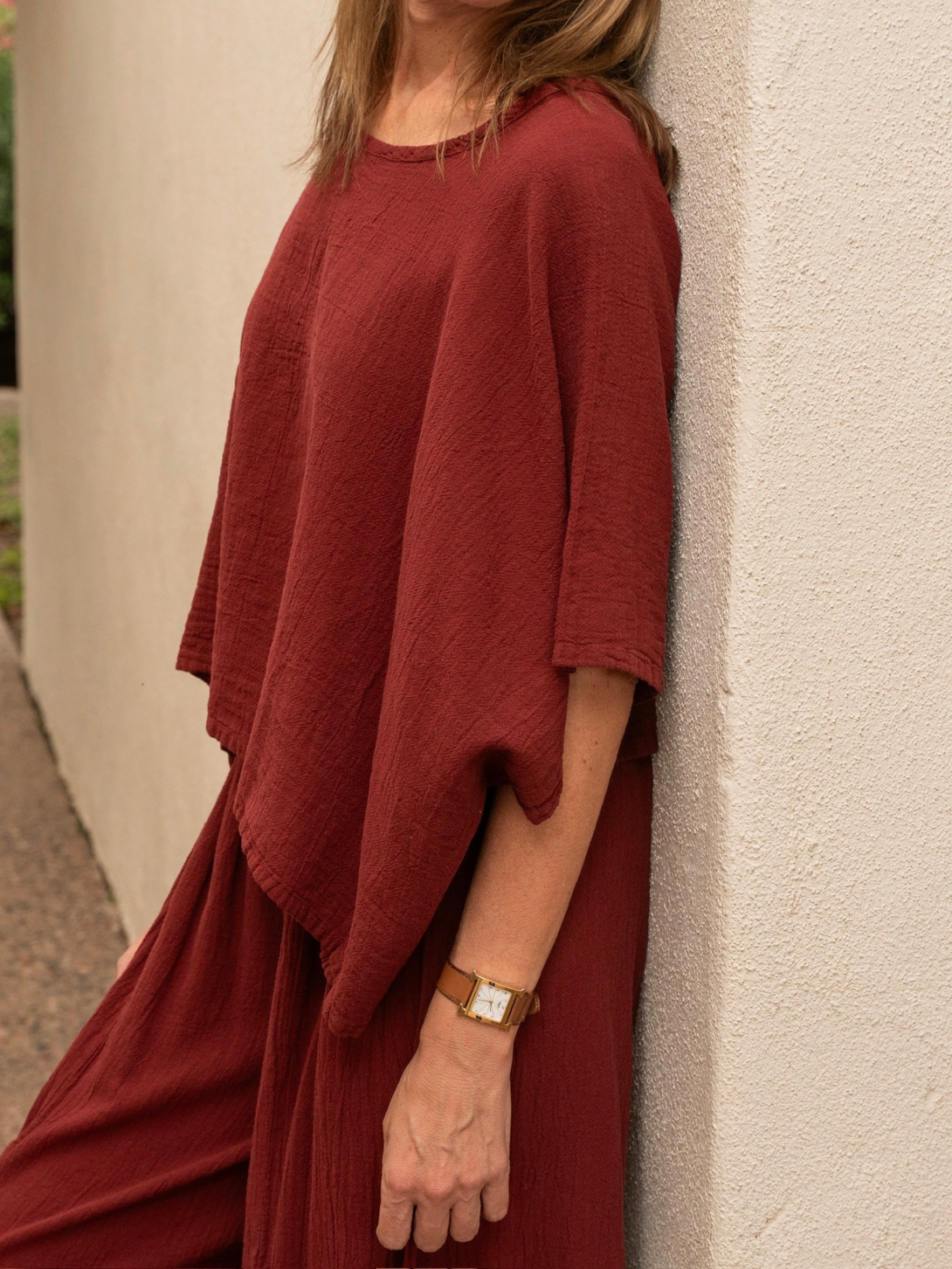Conscious Coterie Carly cotton top in wine red woman leaning against the wall to show the side view of the top