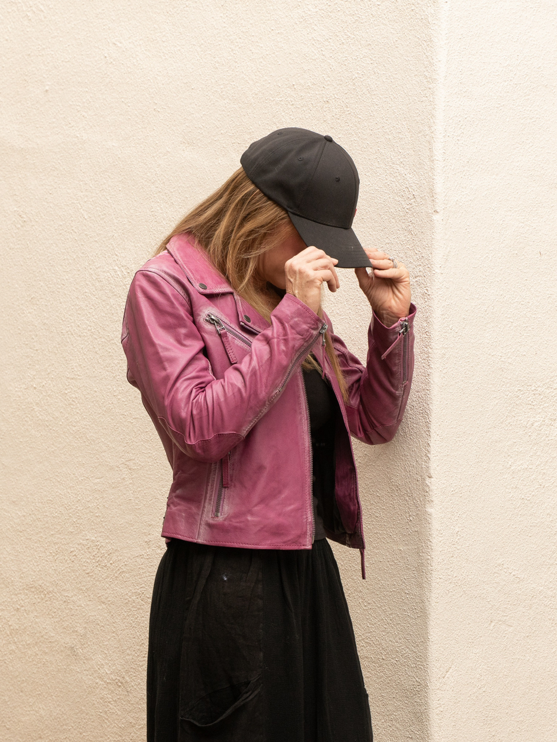 Conscious Coterie Christy star leather jacket in dark pink model holding the hat on her head showing jacket with arms bent