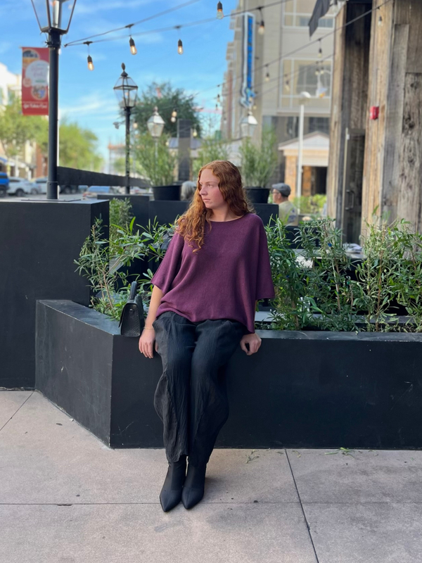Conscious Coterie Katie Sweater in plum photo of woman wearing sweater sitting on a ledge