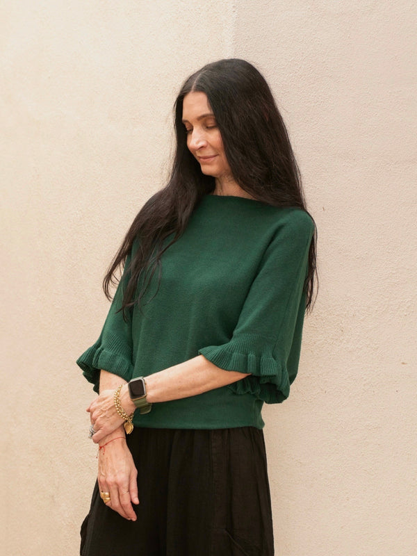 Conscious Coterie Lila Ruffle Sleeve Sweater in forest green on model crossing arms side view