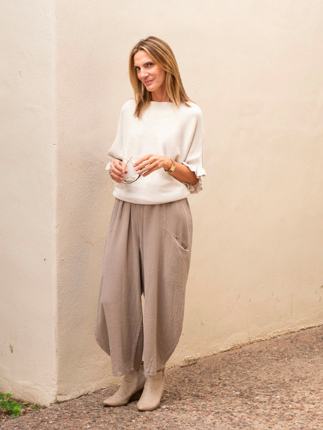 Conscious Coterie Lila Ruffle Sleeve Sweater in light beige on model holding glasses full front view