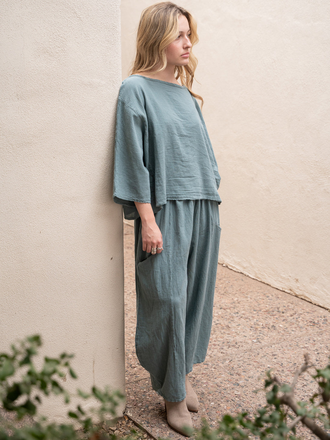 Conscious Coterie Mickey Pant in sea cotton on model leaning against building corner full front side view