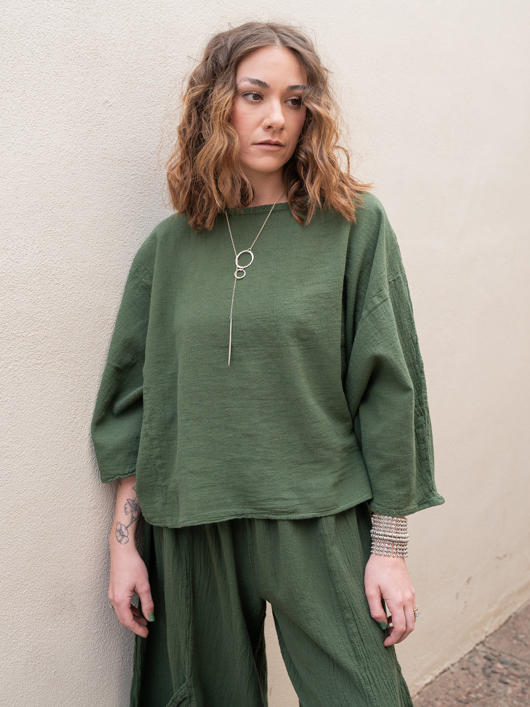 Conscious Coterie Rosie Top in moss cotton on model by wall front view