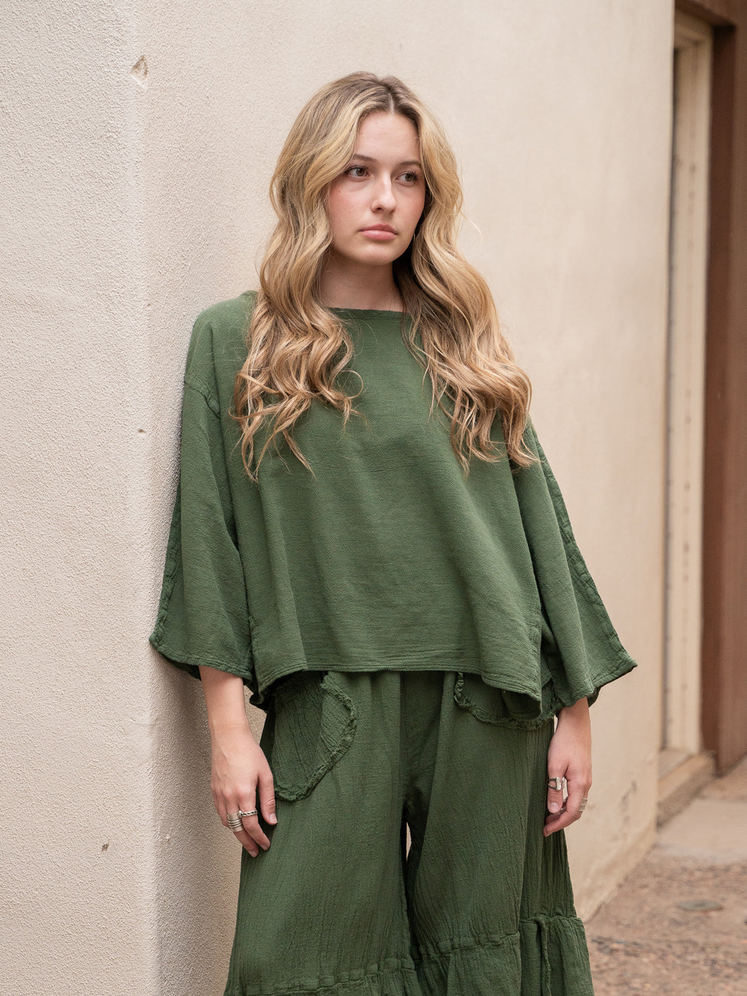 Conscious Coterie Rosie Top in moss cotton on model leaning against wall front view