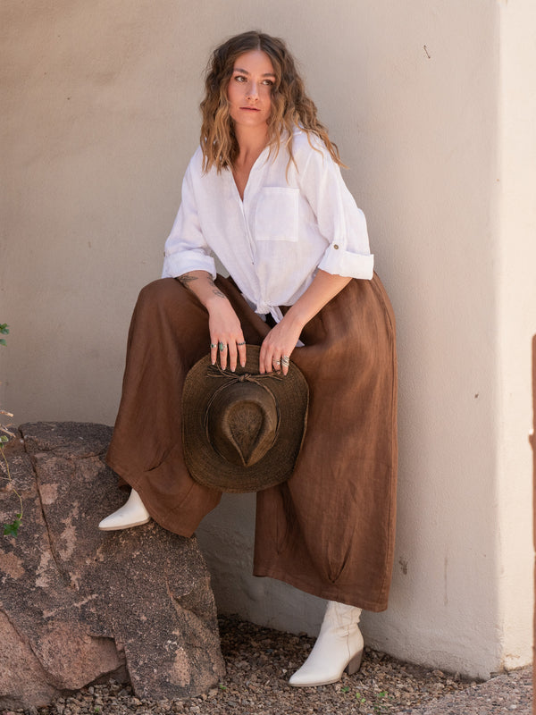 Conscious Coterie Stevie Linen Pant in Coffee on model with foot on rock front view