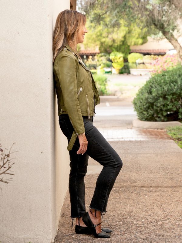 Conscious Coterie Wild Leather Jacket in olive full body photo on woman leaning against the wall displaying side view